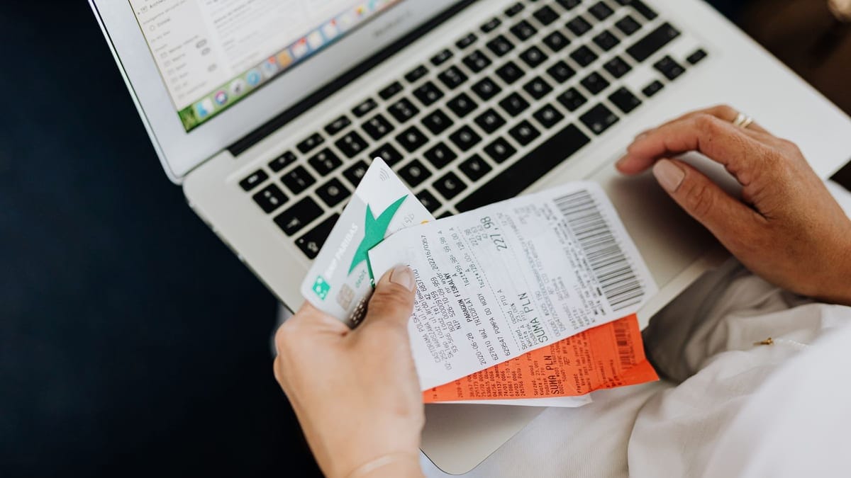 Close-up of hands holding receipts and a bank card in front of a laptop, representing online shopping and e-commerce.