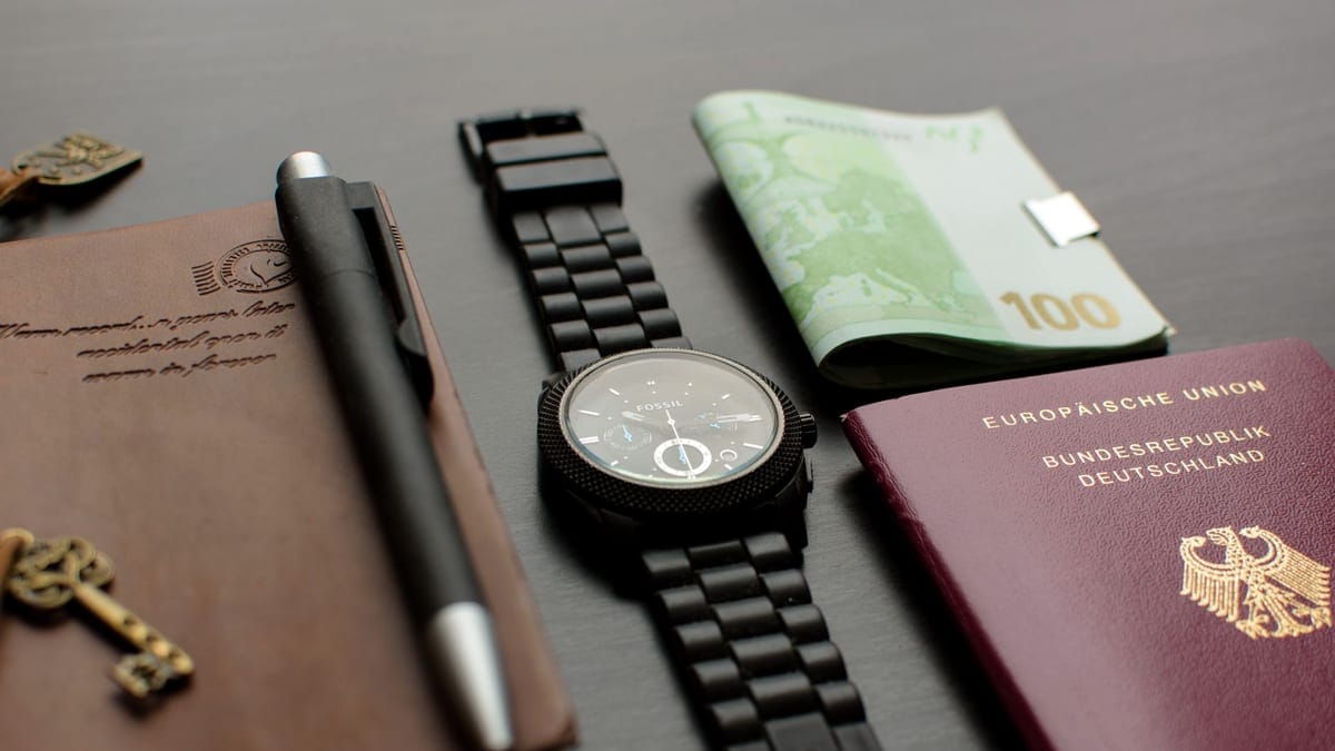 A neatly arranged flat lay depicting essential travel items such as a German passport, wristwatch, and euro bills on a desk.