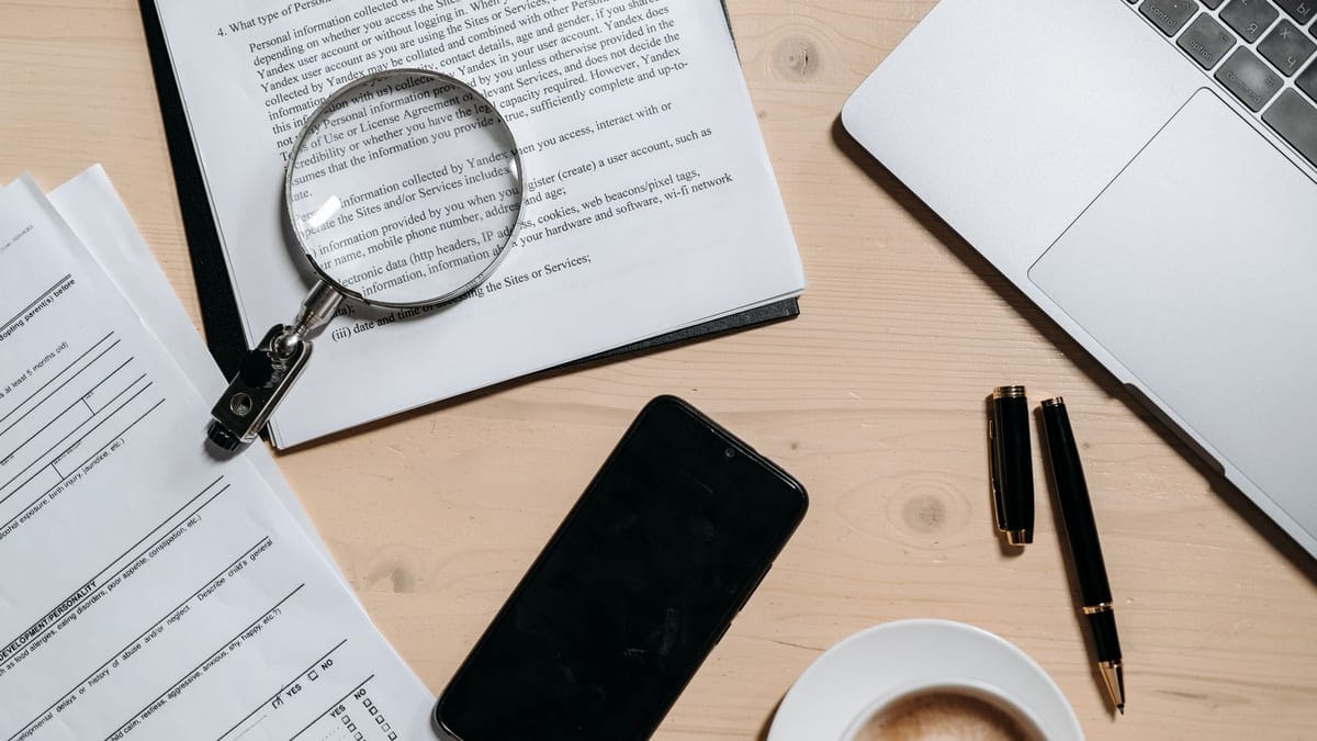 Top view of documents, laptop, coffee, and magnifying glass on office desk.
