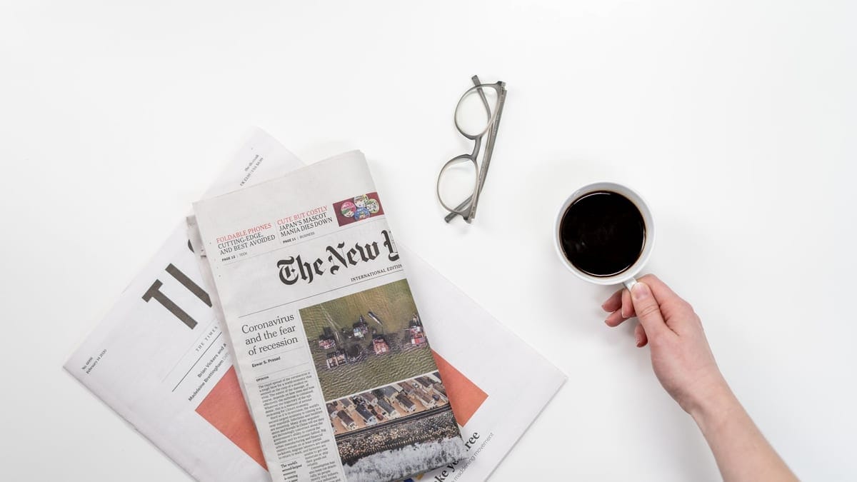 Top view of a coffee cup, newspapers, and eyeglasses on a clean white desk, ideal for a morning routine theme.