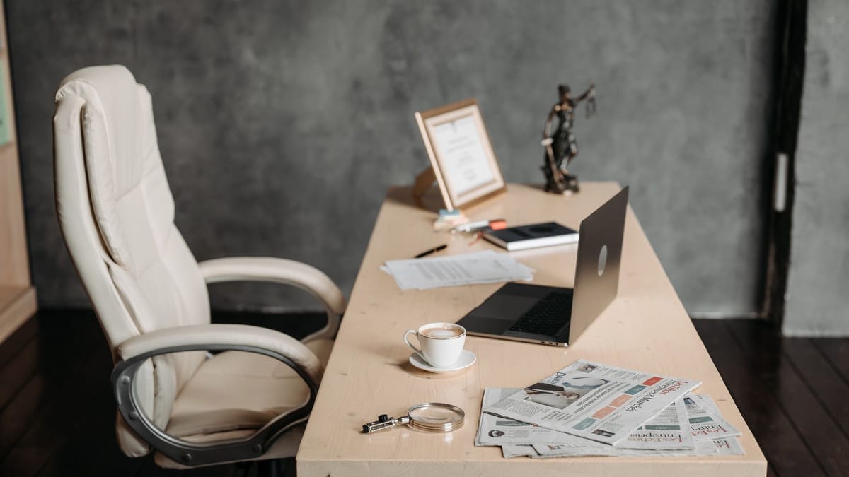 A clean office workspace featuring a cup of coffee, laptop, and newspapers on a wooden desk for a productive environment.