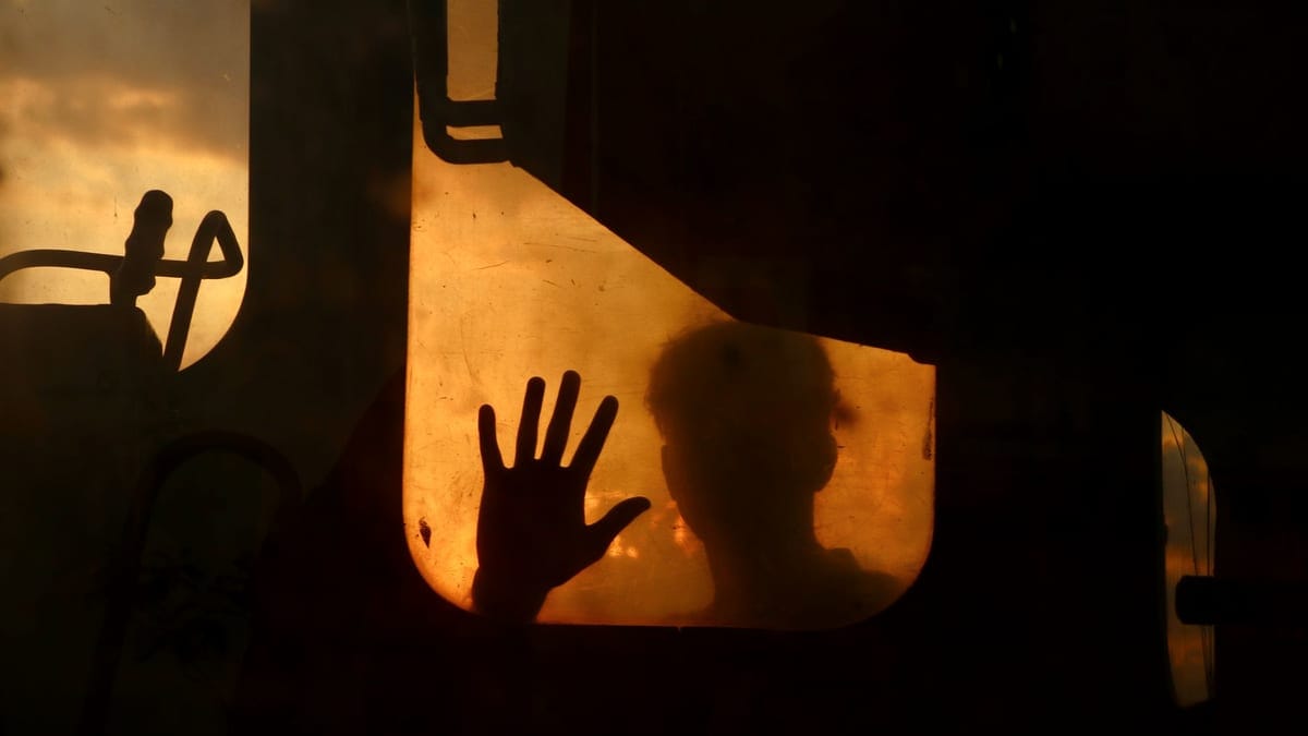 A person’s silhouette with a hand on glass at sunset, creating dramatic shadows.