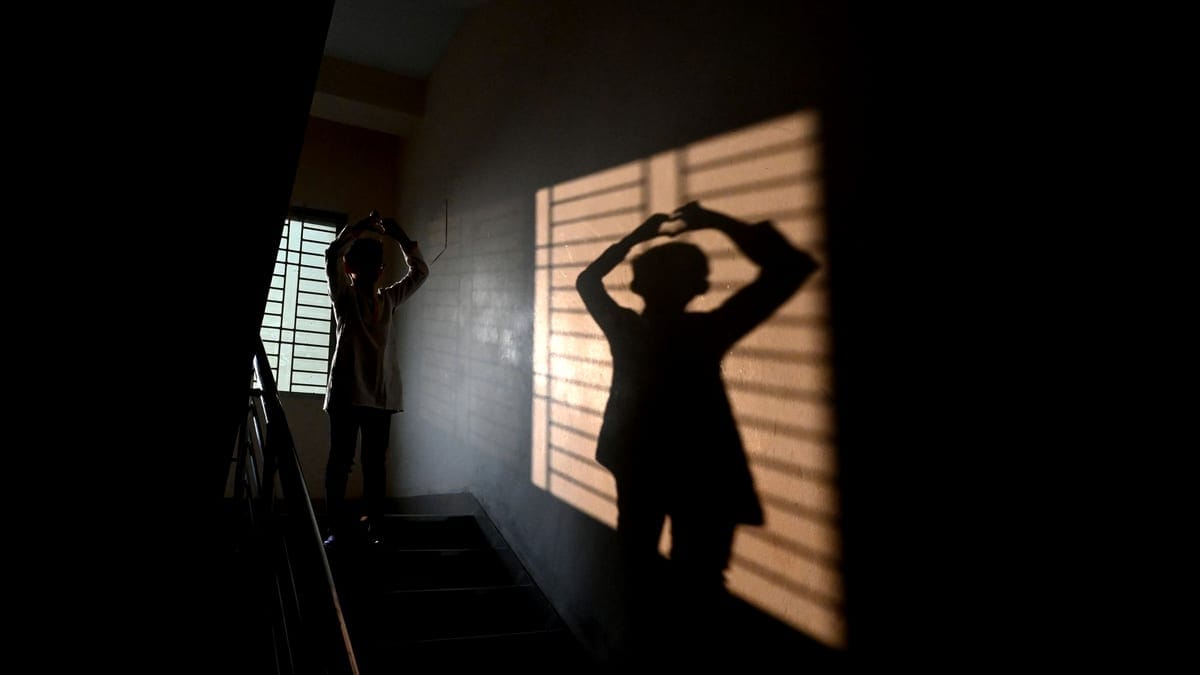 A person creates a silhouette on a stairway with dramatic shadows from a window.