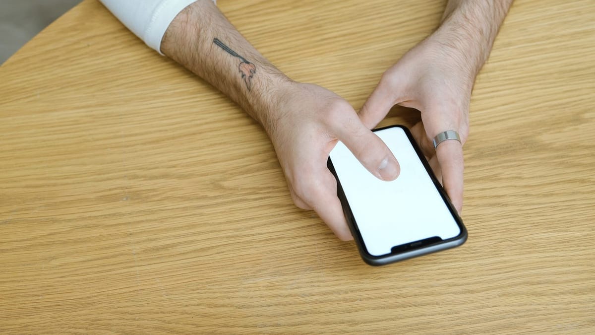 Close-up of hands using a smartphone with a blank screen on a wooden table indoors.