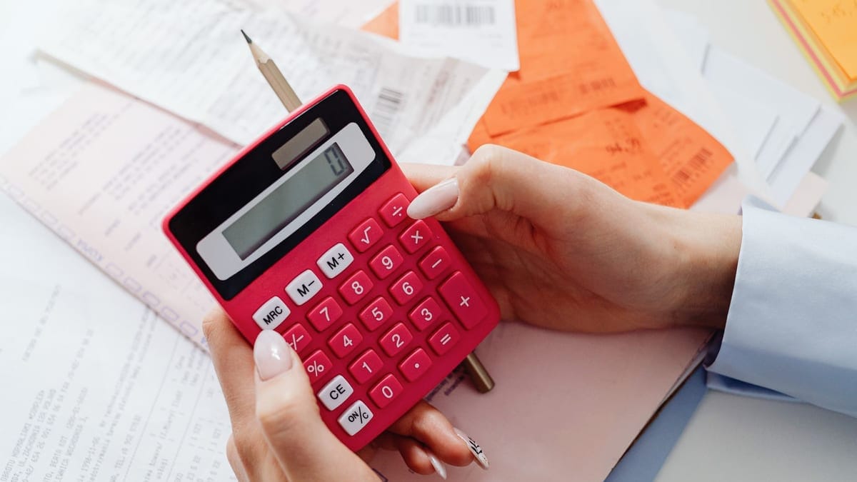 Close-up of hands holding a red calculator, managing finances with documents and receipts.