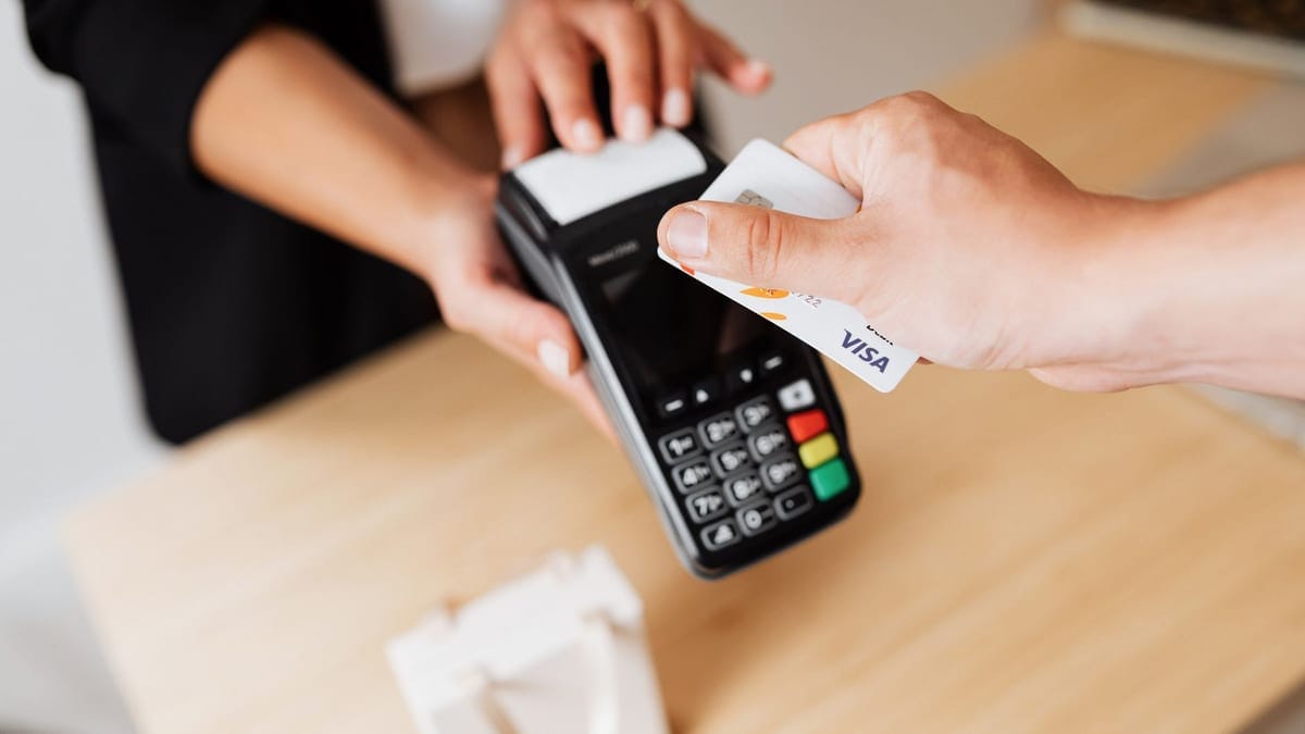 Close-up of hands using a contactless payment terminal with a credit card indoors.