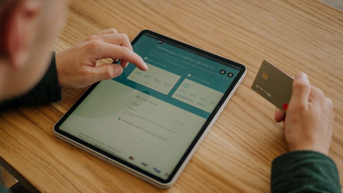 Person making an online payment using a tablet and credit card on a wooden desk.