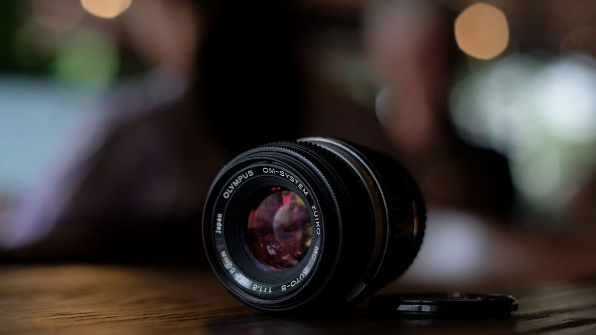 Detailed close-up of a vintage Olympus camera lens resting on a wooden table with bokeh background.