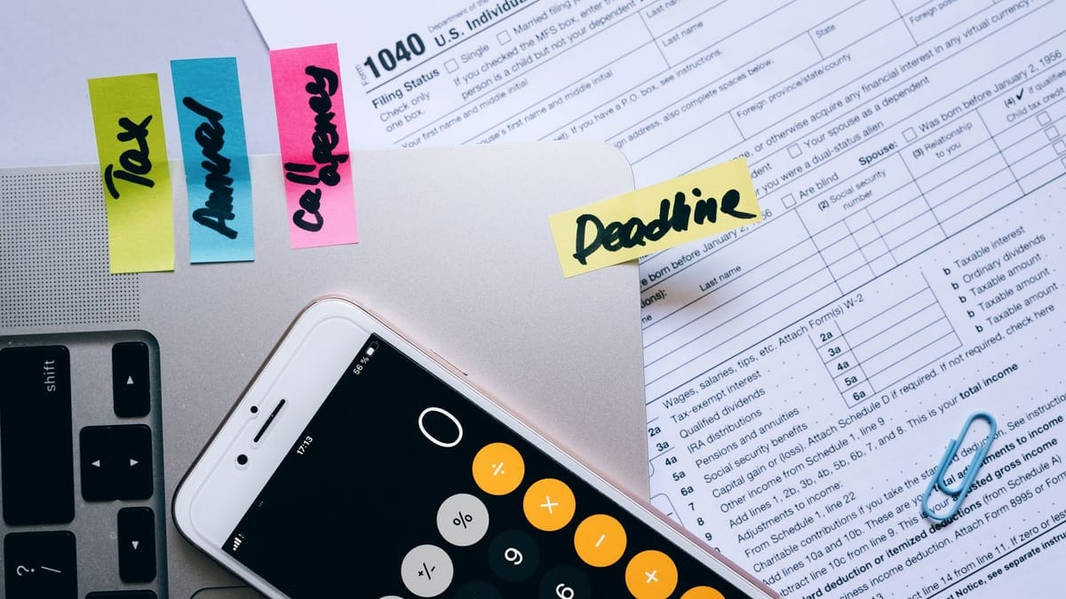 Office desk flat lay showing tax documents, calculator app on smartphone, sticky notes, and paperclips.