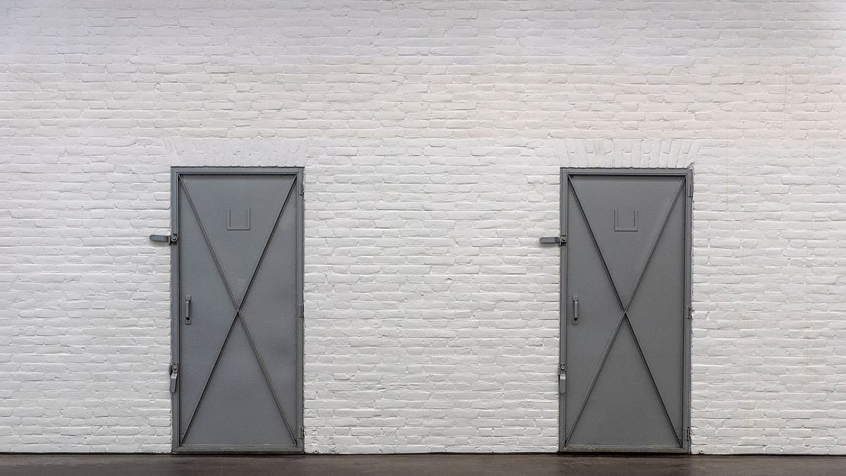 Minimalist photo of two gray metal doors on a white brick wall indoors.