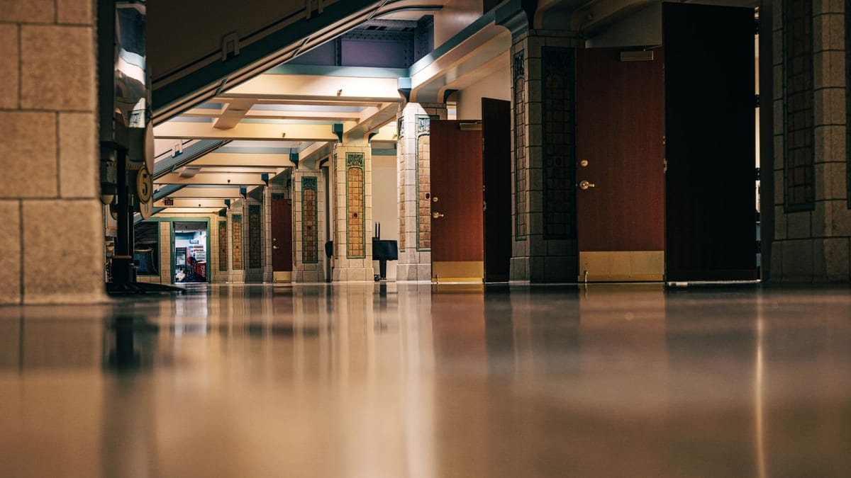 A polished floor reflects lights in an empty corridor with open doors and warm atmosphere.